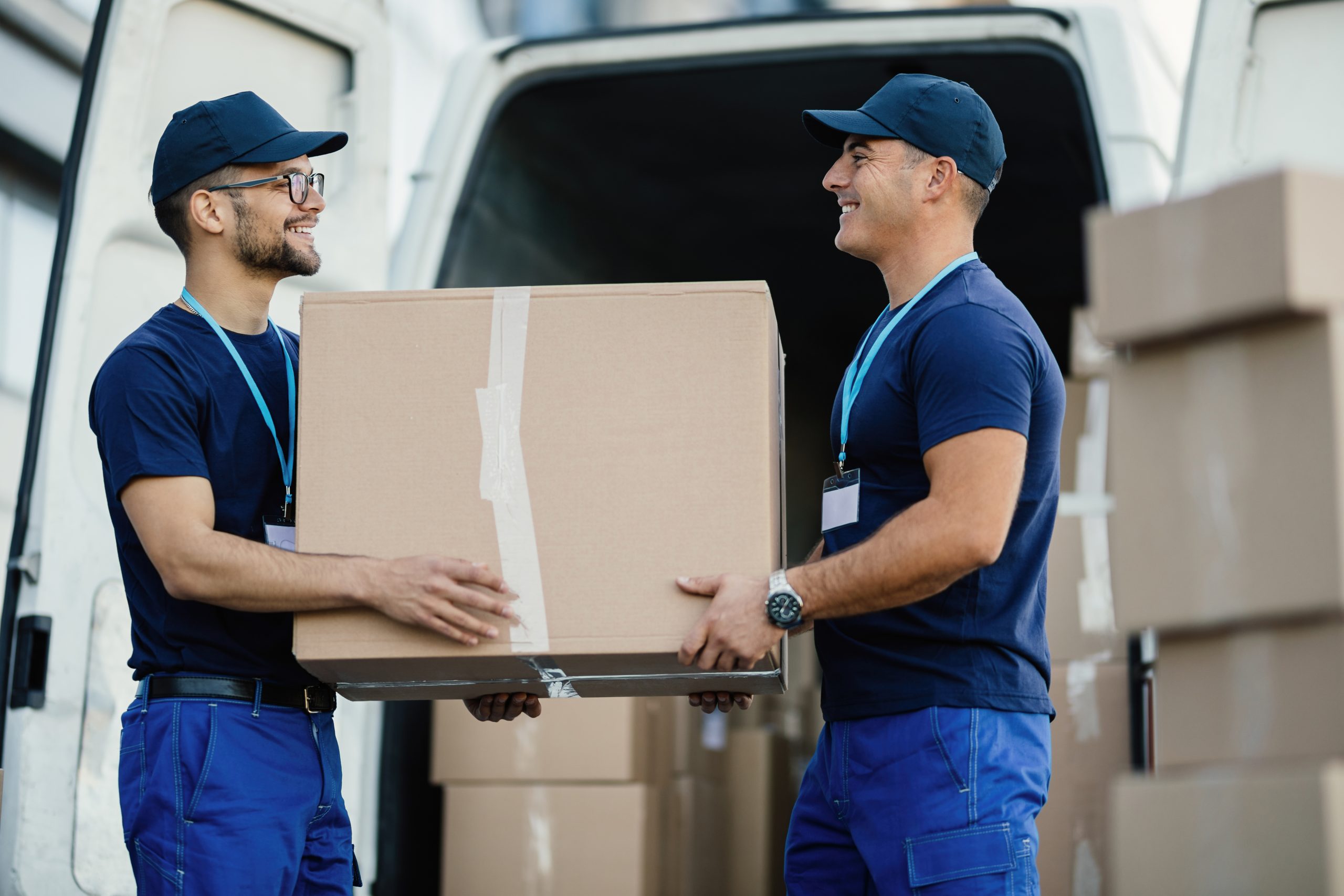 happy manual worker cooperating while carrying cardboard boxes delivery van